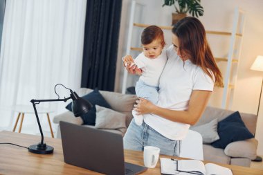 Laptop masanın üstünde. Anne ve küçük kızı evde birlikteler..