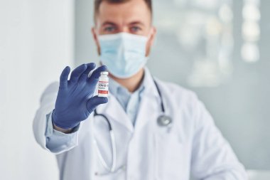 COVID-19 aşısıyla test tüpünü tutuyorum. Klinikte beyaz önlüklü profesyonel doktor var..