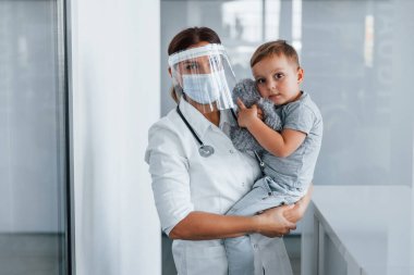 Elinde küçük bir çocukla. Klinikte beyaz önlüklü profesyonel doktor var..