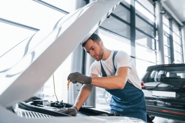 Kaliteli hizmet. Beyaz gömlekli ve mavi üniformalı genç adam otomobil tamir ediyor..