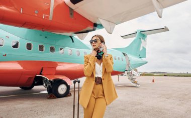 Sarı elbiseli. Bagajlı genç bayan dışarıda, uçağın yanında..