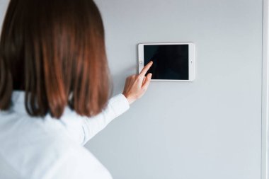 Duvara monte edilmiş tablet kullanıyor. Genç bayan gündüz vakti akıllı ev odasında..