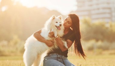 Bina arka planda. Köpeğiyle bir kadın güneşli bir günde sahada eğleniyor..