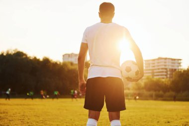 Ayakta duruyor ve topu elinde tutuyor. Genç futbolcu spor sahasında antrenman yapıyor..
