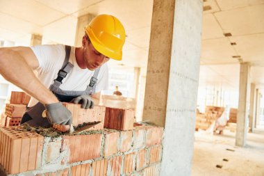 Tuğla kullanarak çalışmak. Gündüz vakti inşaatta üniformalı genç bir adam..
