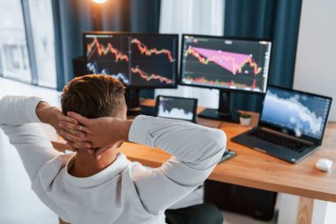 Dinleniyorum. Resmi giyinmiş genç işadamı birden fazla ekranla ofiste..