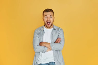 Stüdyoda turuncu arka planda duran günlük kıyafetli genç adam..