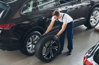 Tekerlek değiştirme. Beyaz gömlekli ve mavi üniformalı genç adam otomobil tamir ediyor..