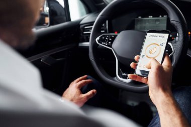 Arabada oturuyordu. Etiketli ve simgeli telefonları tutan adamın elini yakından izle. Uzaktan kumanda kavramı.