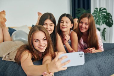 Akıllı telefonla yatağa uzanmak. Bir grup mutlu kadın bekarlığa veda partisindeler..