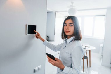 Duvara monte edilmiş tablet kullanıyor. Genç bayan gündüz vakti akıllı ev odasında..