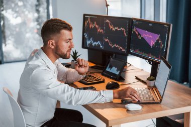 Laptop kullanıyorum. Resmi giyinmiş genç işadamı birden fazla ekranla ofiste..