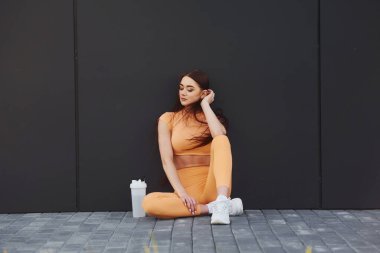 Oturup dinleniyor. Spor giyimli genç bir kadının dışarıda spor seansı var..