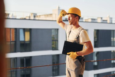 Proje yöneticisi. Gündüz vakti inşaatta üniformalı genç bir adam çalışıyor..
