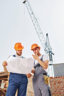 Okuma planı. Üniformalı iki genç inşaat işçisi tamamlanmamış binada meşgul..