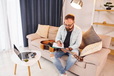 Şarkı yapıyorum. Gündelik giysiler içinde ve akustik gitarlı bir adam içeride..