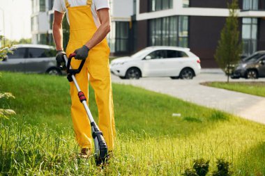 Arka planda dış bina inşa ediliyor. Bahçede çimleri çim biçen bir adam var..