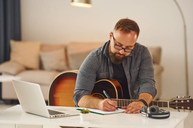 Bazı fikirler yazıyorum. Gündelik giysiler içinde ve akustik gitarlı bir adam içeride..