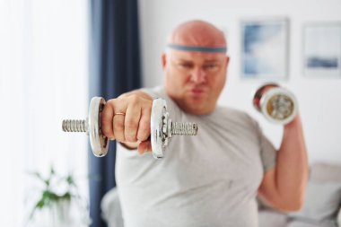 Dambıl kullanıyor. Sıradan giysili komik şişman adam evde..