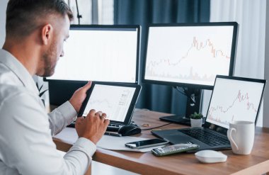 Modern teknolojiler. Resmi giyinmiş genç işadamı birden fazla ekranla ofiste..