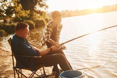 Hobi kavramı. Baba ve oğul yazın birlikte açık havada balık avlıyorlar..