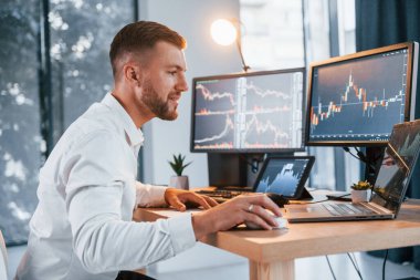 Borsa. Resmi giyinmiş genç işadamı birden fazla ekranla ofiste..
