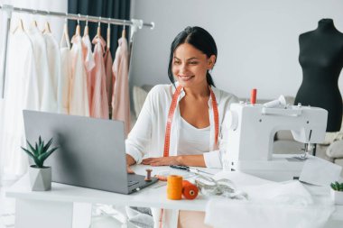 Beyaz renkli dikiş makinesi. Terzi odasında, farklı kıyafetlerle..