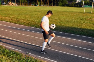 Topu elinde tutuyor. Genç futbolcu spor sahasında antrenman yapıyor..