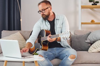 Şarkı yazma süreci. Gündelik giysiler içinde ve akustik gitarlı bir adam içeride..