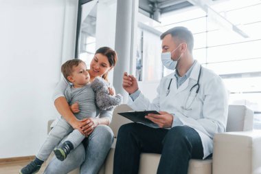 Küçük çocuk inceleniyor. Beyaz önlüklü iki doktor klinikte birlikte çalışıyorlar..