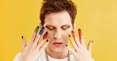 Genç eşcinsel adam stüdyoda duruyor ve kameraya poz veriyor. Sarı arkaplan.