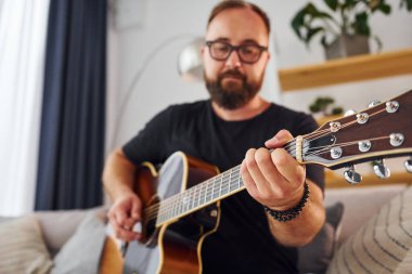 Enstrüman çalıyorum. Gündelik giysiler içinde ve akustik gitarlı bir adam içeride..