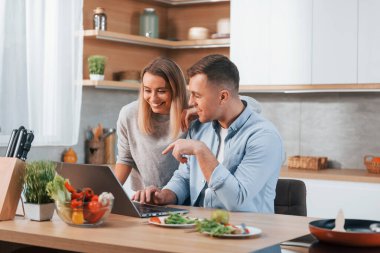 Laptopa bakıyorum. Modern mutfakta yemek hazırlayan bir çift..