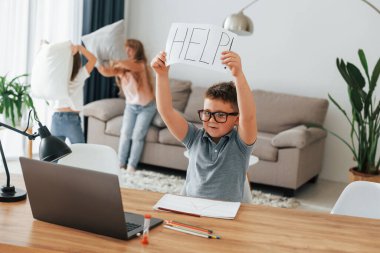 Elinde yardım sözcüğüyle kağıt tutan çocuk. Ders almayı reddediyor. Çocuklar gündüz vakti evlerinde eğleniyorlar..