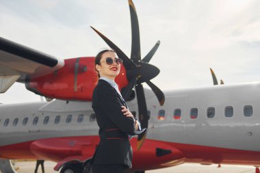 Resmi siyah elbiseli genç hostes uçağın yanında dikiliyor..