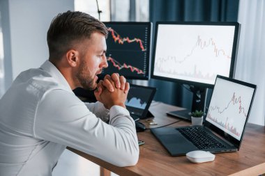 İşime odaklanıyorum. Resmi giyinmiş genç işadamı birden fazla ekranla ofiste..