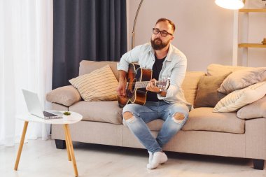 Sıcak bir atmosfer. Gündelik giysiler içinde ve akustik gitarlı bir adam içeride..