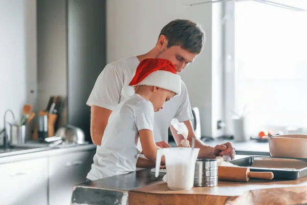 Eggs, milk and dough. Father teaching his little son with preparing of sweet christmas cookies.