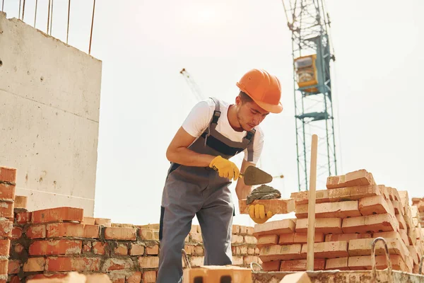 Young construction worker in uniform is busy at the unfinished building.