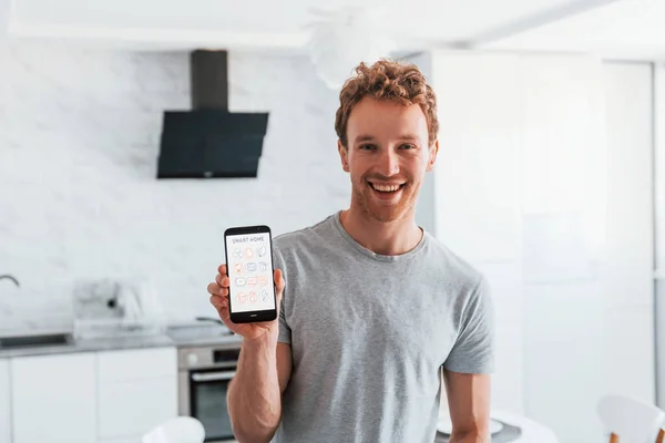 Young man in casual clothes is indoors controlling smart home technology.
