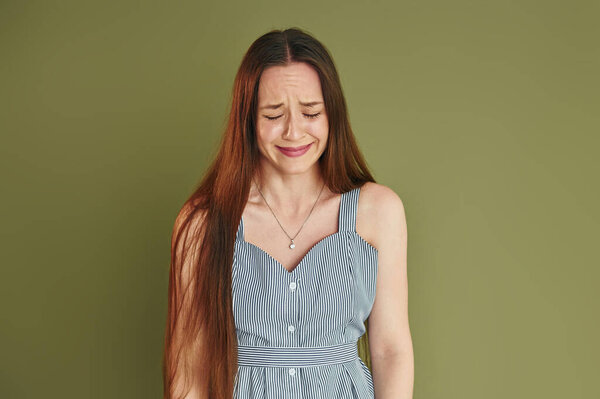 Young woman in casual clothes is crying while standing indoors in the studio.