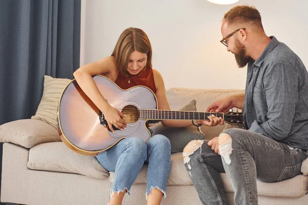 Guitar teacher showing how to play the instrument to young woman.