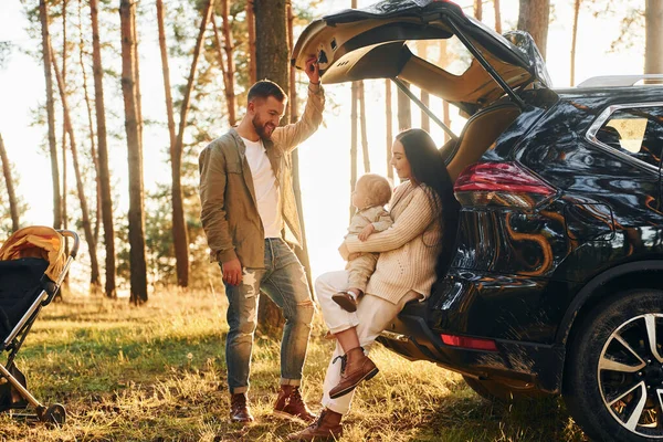 黒い色の自動車で 父と母と娘の幸せな家族が森の中にいる — ストック写真