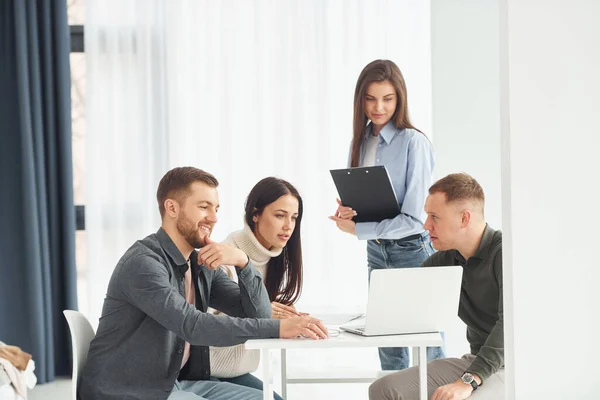 Four people works in the office by sitting by the table indoors.