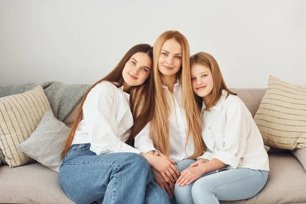 坐在沙发上 年轻的母亲白天带着两个女儿在家里 — 图库照片
