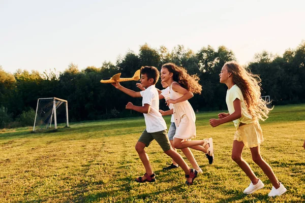 和玩具飞机一起跑步一群快乐的孩子白天在运动场上玩耍 — 图库照片