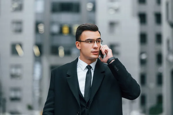 通过电话交谈 穿着黑色西装打领带的商人在城市的户外 — 图库照片