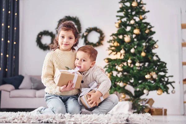 带着礼品盒小弟弟和小妹妹在圣诞节装饰房间里 — 图库照片