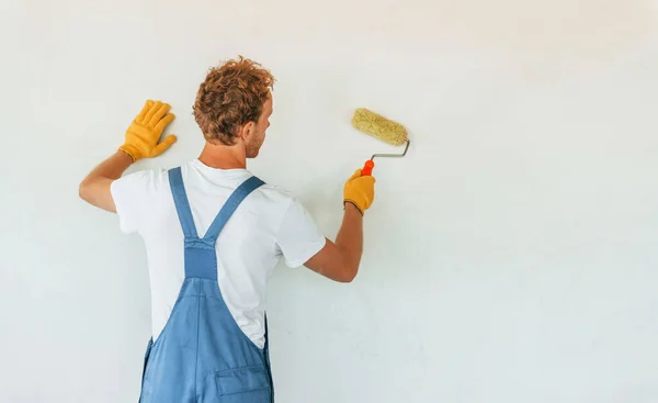 stock image Clean walls. Young man working in uniform at construction at daytime.