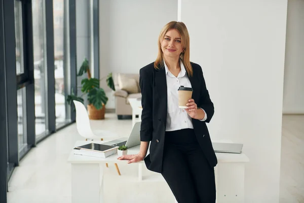 Woman in formal clothes is indoors in the modern office at daytime.